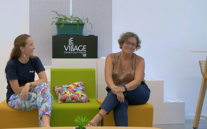 Deux femmes assises sur des banquettes colorées dans un espace de coworking, devant un panneau Le Village