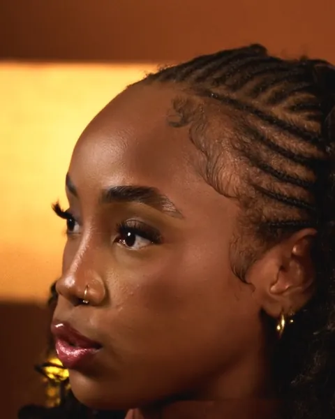 Portrait de profil d'une femme aux cheveux tressés, éclairée d'une lumière orangée