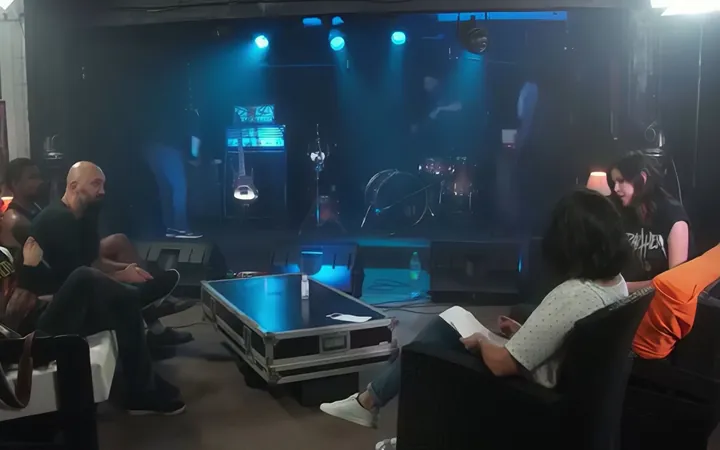 Plateau de concert éclairé de bleu, avec batterie, spectateurs et deux femmes assises au premier plan